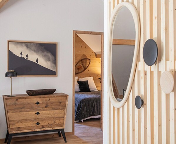 Ein Schlafzimmer mit einem Holzkoffer, einem Bett mit dunkelblauer Bettdecke, einem großen, ovalen Spiegel und einem Gemälde von einer Berglandschaft.