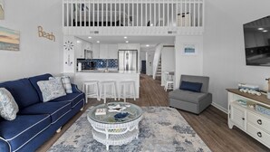 A spacious living area with a blue sofa, a glass coffee table, and a white dining set. - Charming 2-bedroom condo with fitness room, WiFi in awesome Surf City (Surf City)