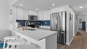A modern kitchen with white cabinets, a stainless steel refrigerator, a microwave, and a marble island with bar stools. - Charming 2-bedroom condo with fitness room, WiFi in awesome Surf City (Surf City)