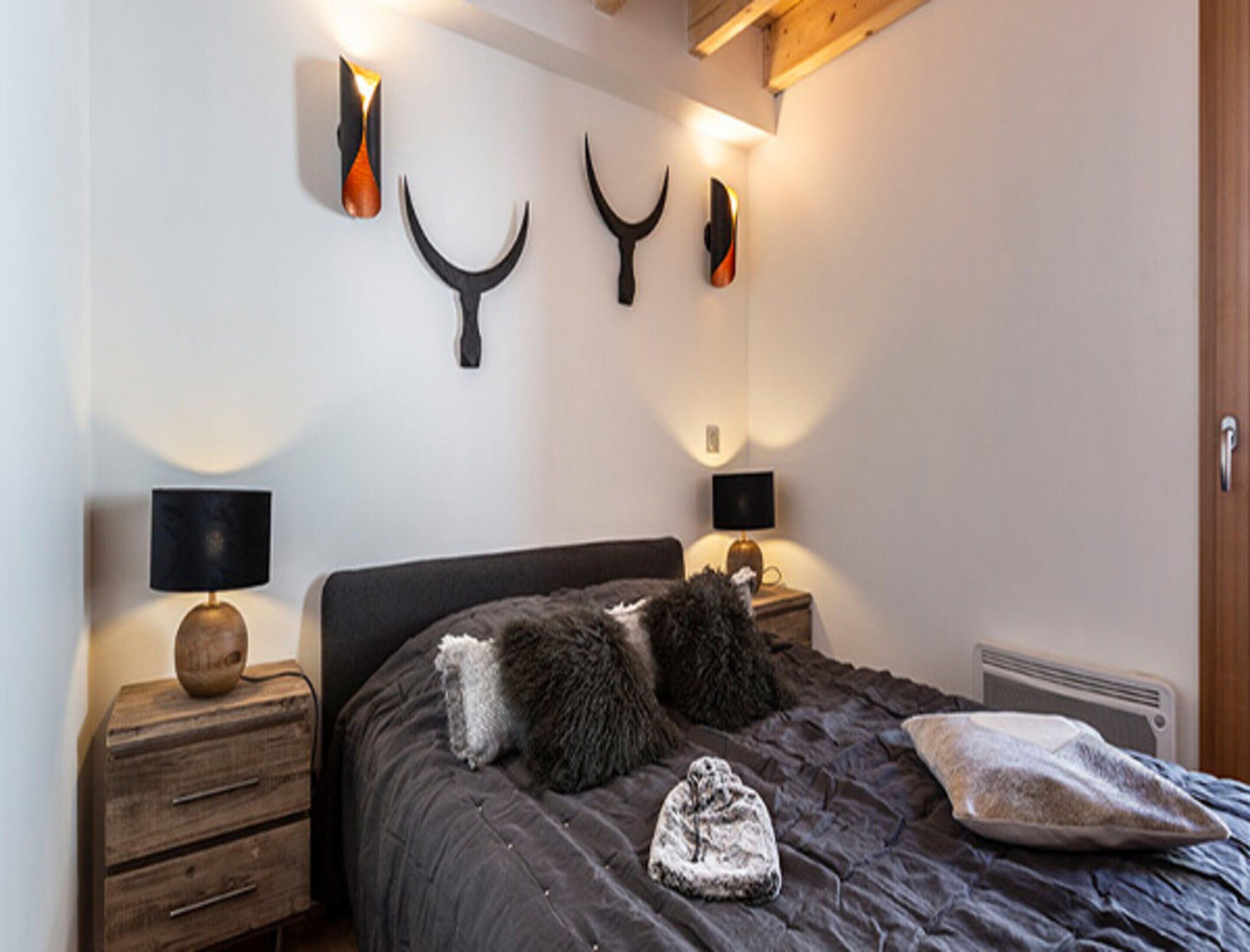 A bedroom with a dark-colored bed, two bedside tables with lamps, and wall-mounted decor.