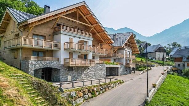 A multi-story chalet with stone walls, wooden balconies, and a mountain backdrop. - Apartment in Vaujany Near Alpe D'huez (Vaujany)