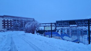 Una strada innevata con edifici e una recinzione.