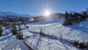 Paesaggio innevato con cielo sereno, una recinzione in legno e una montagna sullo sfondo.