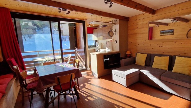 Accogliente interno di una baita con zona pranzo, divano e vista attraverso la porta vetrata.