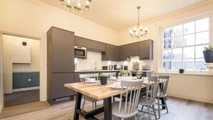 Une cuisine moderne avec une table à manger en bois, des chaises blanches et une grande fenêtre donnant sur des immeubles.