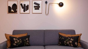 A grey sofa with floral cushions, a wall-mounted lamp, and three framed abstract artworks. - Hotel Tinah: Elegance and Comfort Near the Champs-elysees (Paris)