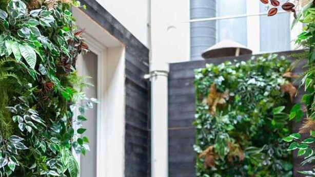 A modern outdoor area with a wooden deck, a vertical garden, and neatly trimmed bushes. - Hotel Tinah: Elegance and Comfort Near the Champs-elysees (Paris)