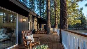 A wooden deck with outdoor seating, a dining area, and a view of tall pine trees.
