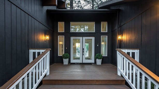 A wooden staircase leading to a dark-colored entrance with two doors and potted plants on either side.