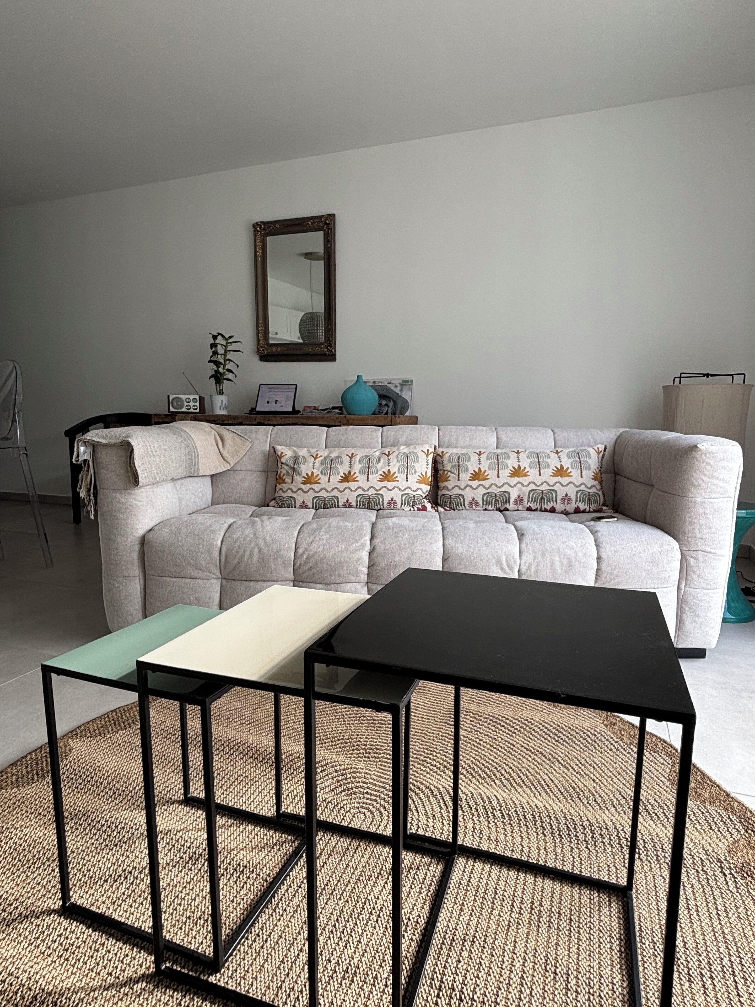 A living room with a grey sofa, two black tables, a woven rug, and a mirror on the wall.