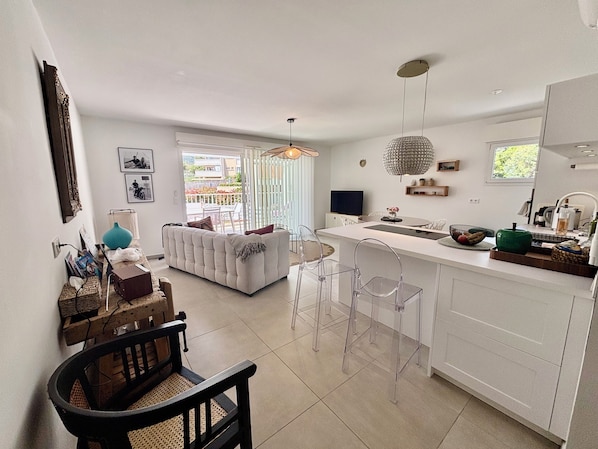 A modern kitchen with a dining area, a sofa, and a TV.