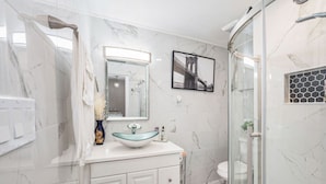 Ein modernes Badezimmer mit einer Duschkabine aus Glas, einem weißen Marmorwaschbecken und einem gerahmten Bild an der Wand.