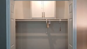 Ein kleiner, abgeschlossener Schrank mit weißen Türen, einer Kleiderstange und einem Sessel mit Decke.