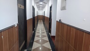 A long, narrow hallway with a checkered floor pattern, flanked by walls with vertical wooden panels and a ceiling with recessed lighting. - Hotel Pearl (Haridwar)