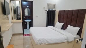A hotel room with a bed, a bedside table with a phone, a small sink, and a mirror. - Hotel Pearl (Haridwar)