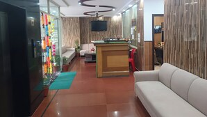 A modern hotel lobby with a reception desk, seating area, and a ceiling fan. - Hotel Pearl (Haridwar)