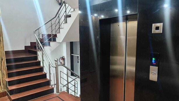 A modern elevator with a control panel, a staircase with metal railings, and a fire extinguisher on the wall. - Hotel Pearl (Haridwar)
