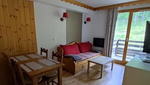 A cozy room with a wooden dining table, a sofa with red cushions, and a TV on a stand. - 200m from ski slopes, view ski slopes, swimming pool, sauna, tv, ski locker, 35m², Les Orres (Les Orres)
