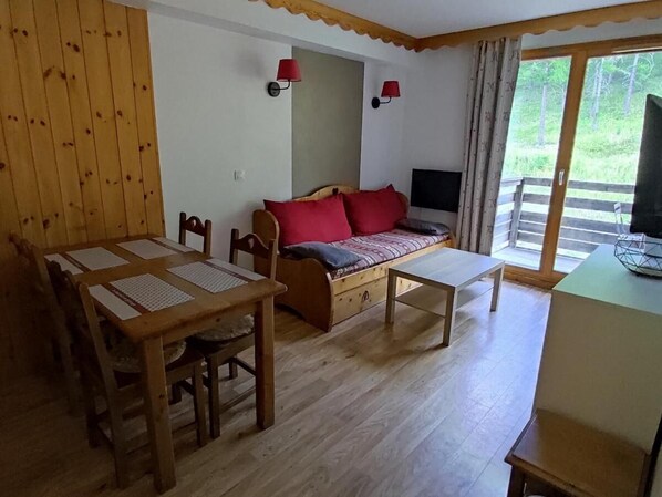 A cozy room with a wooden dining table, a sofa with red cushions, and a TV on a stand. - 200m from ski slopes, view ski slopes, swimming pool, sauna, tv, ski locker, 35m², Les Orres (Les Orres)