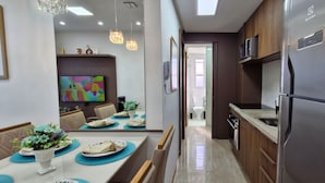 A modern kitchen with a built-in refrigerator, microwave, and oven. There is a dining area with a table set for two, a vase of flowers, and a colorful painting on the wall. - COCAZ0106 - Smart Sol do Costa Azul (Salvador)