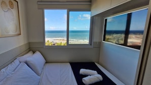 A small, single-bed room with a window overlooking a beach and ocean. - COCAZ0106 - Smart Sol do Costa Azul (Salvador)
