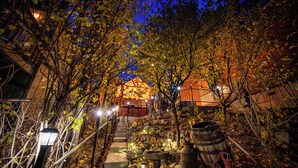 A stone pathway leading to a building with a traditional roof, surrounded by trees and illuminated by ground lights. - Secluded Cabin w/ Spa & Games! (Big Bear)