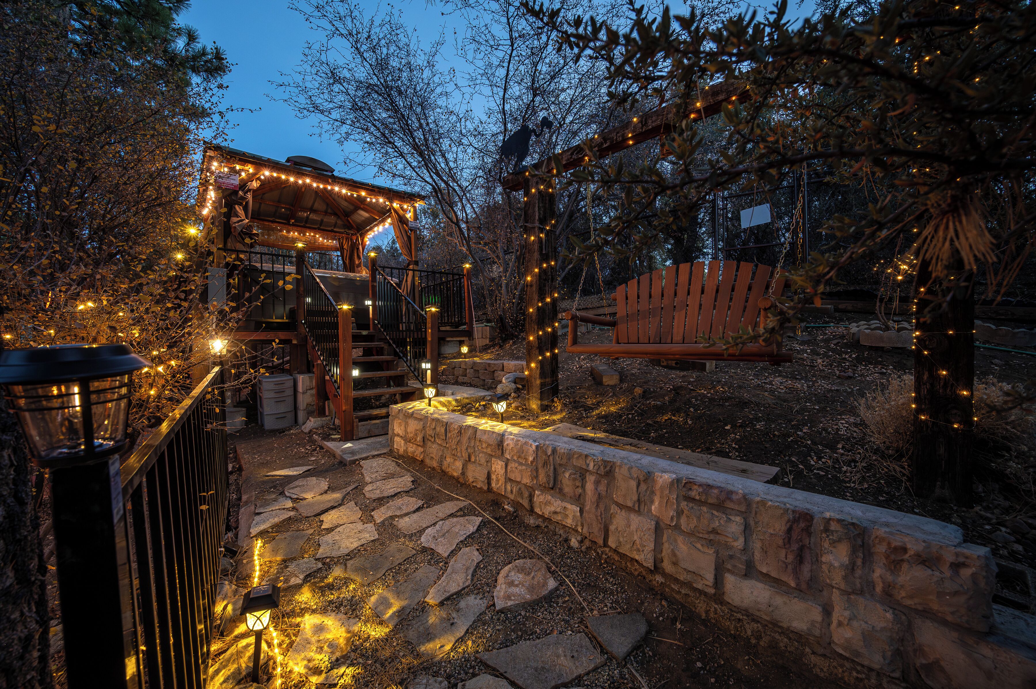 A stone pathway leading to a wooden gazebo with string lights.