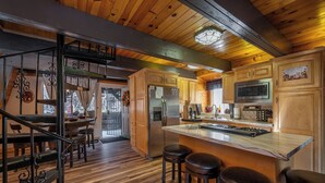 A kitchen with wooden cabinets, a stainless steel refrigerator, a microwave, and a large island with stools. - Secluded Cabin w/ Spa & Games! (Big Bear)