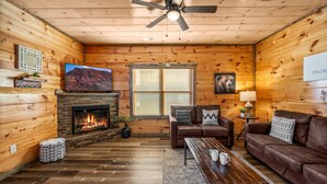 Ein gemütliches Blockhaus-Interieur mit Kamin, Holzwänden, einer Ledersofa und einem Fernseher.