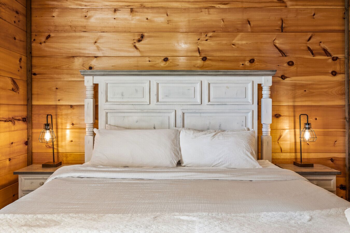Una cama con cabecera blanca, dos mesitas de noche y dos lámparas de pared.