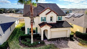 A two-story house with a tiled roof, a garage, and a well-maintained lawn with a palm tree.