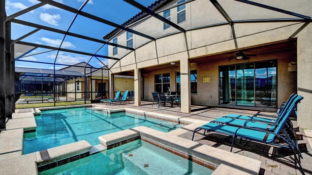 A swimming pool area with lounge chairs, a covered patio, and a building with large windows.
