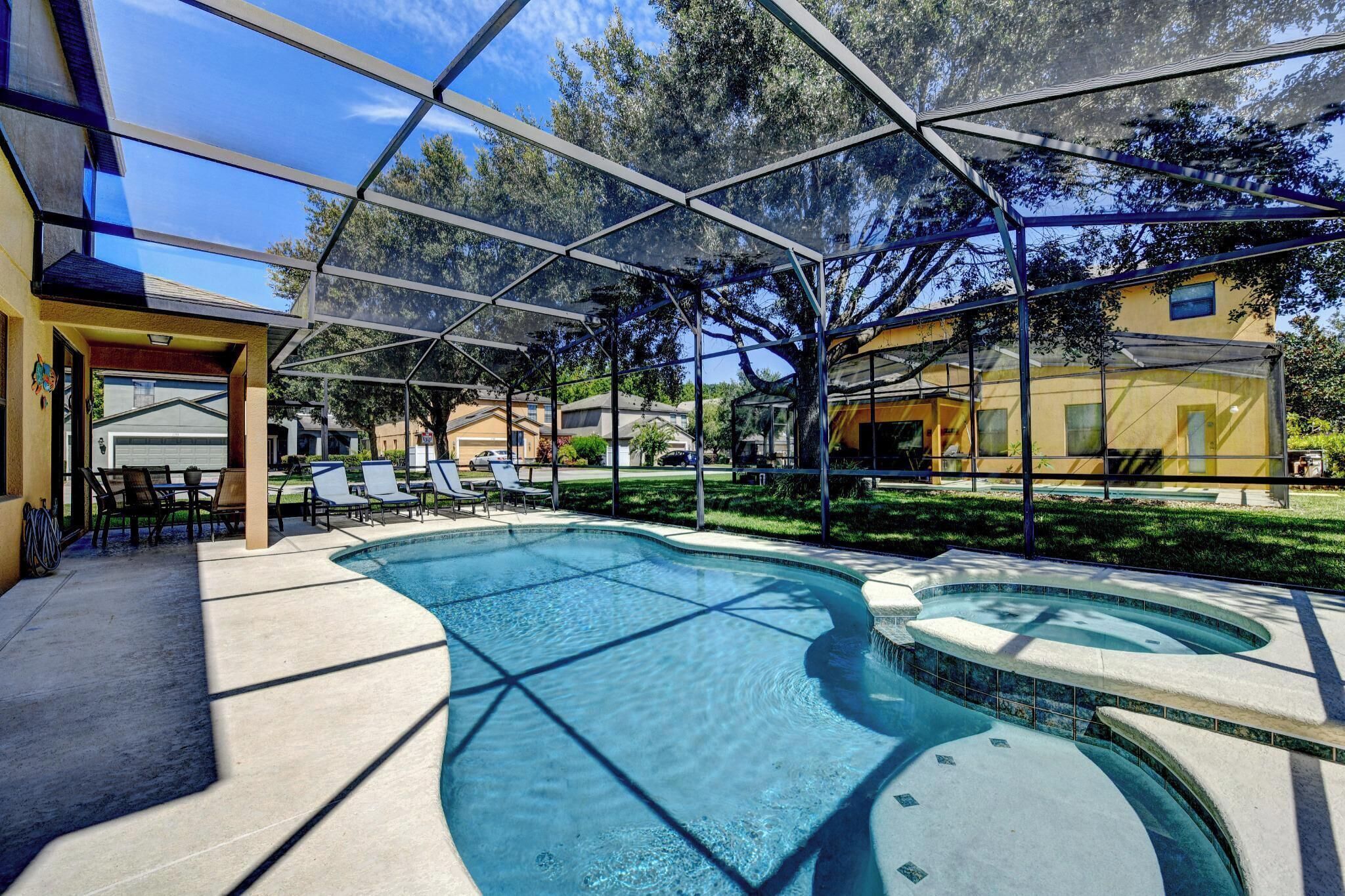 Ein Schwimmbecken mit Glasüberdachung, umgeben von Liegestühlen und einer Terrassenfläche.