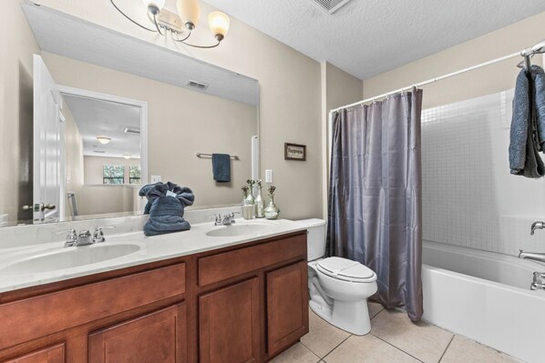 A bathroom with a double sink vanity, a toilet, and a bathtub with a shower curtain.