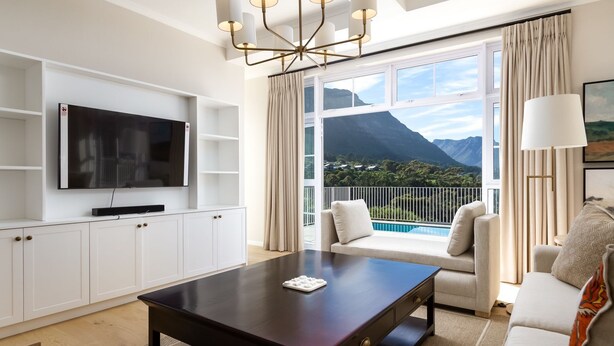 Un salon moderne doté d’un téléviseur à écran plat, d’une table basse en bois foncé, d’un canapé et d’un balcon offrant une vue sur les montagnes.