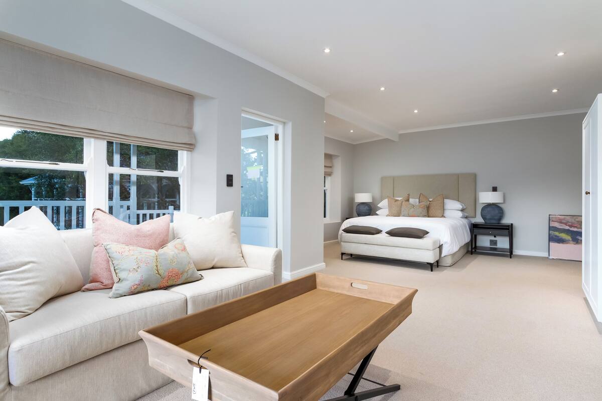 A modern bedroom with a large bed, a bedside table, and a nightstand. There is a window with a view of the outside.