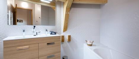 A modern bathroom with a wooden vanity, a large mirror, a bathtub, and a small wicker basket.