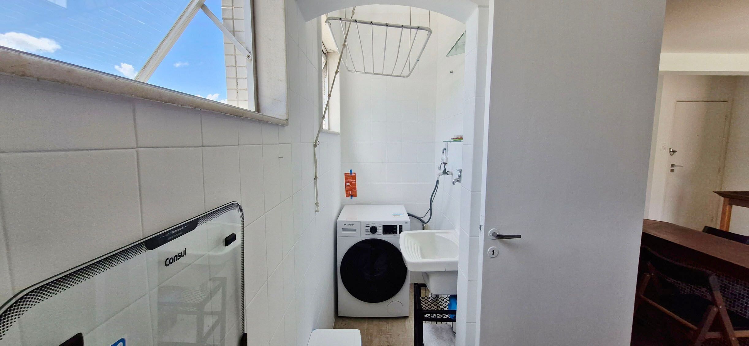 A compact laundry room with a washing machine, a drying rack, and a sink.