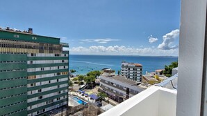 A high-rise building with multiple balconies overlooking a coastal area with boats and a clear sky. - COBAR0130 - Edifício Porto do Sol (Salvador)