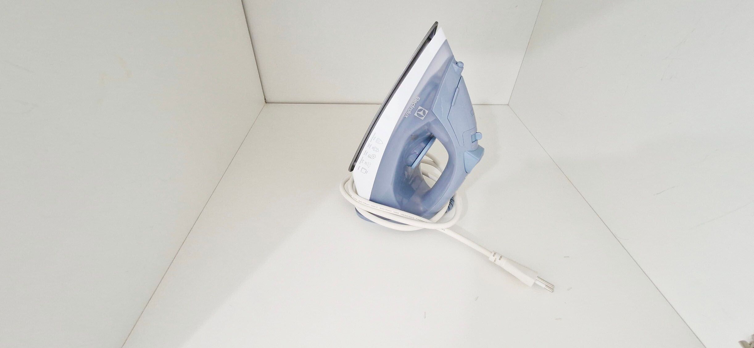 Una plancha con cable enchufada, sobre una superficie blanca.
