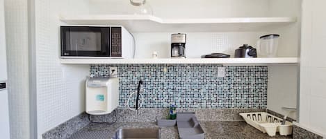 Cocina compacta con microondas, cafetera y licuadora en la encimera.