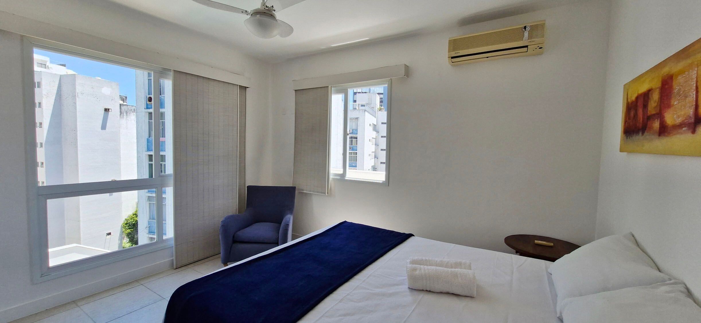 A hotel room with a bed, a chair, and a large window.