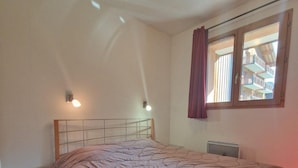 Une chambre à coucher avec un lit, une petite table, une fenêtre avec des rideaux et un luminaire au plafond.