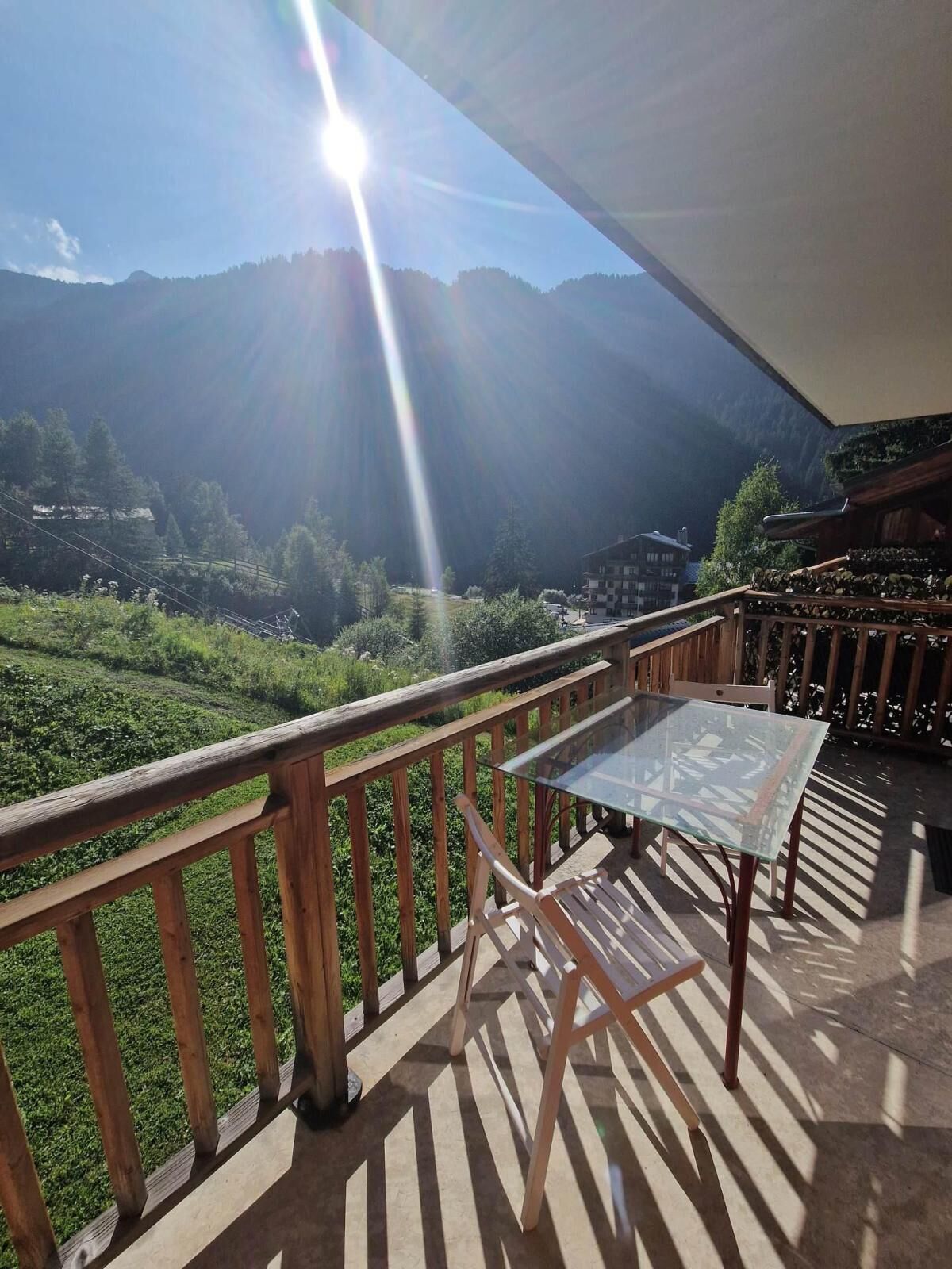 Varanda com mesa e cadeiras de vidro, com vista para uma paisagem montanhosa.