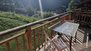 Un balcon avec une table et des chaises en verre, donnant sur un paysage montagneux.