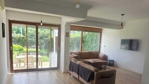 A spacious room with a large sliding glass door leading to an outdoor area, a wooden floor, and a brown sofa. - VILLA OLINDA 4 BED with huge garden (Serik)