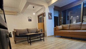A spacious living room with a wooden floor, two sofas, a coffee table, and a large window providing a view of the outside. - VILLA OLINDA 4 BED with huge garden (Serik)