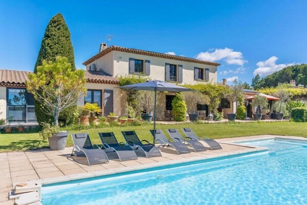 Blick auf ein Haus mit Pool, Liegestühlen und einer Terrassenanlage.