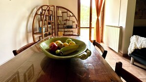 A dining area with a wooden table, a green bowl with fruits, and a bookshelf. - Milu's Holiday Home (Toscana)