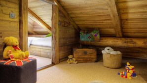 Una habitación acogedora en el ático, con techo de madera, una cama, un osito de peluche, un aparador, una cesta con un peluche y un libro.